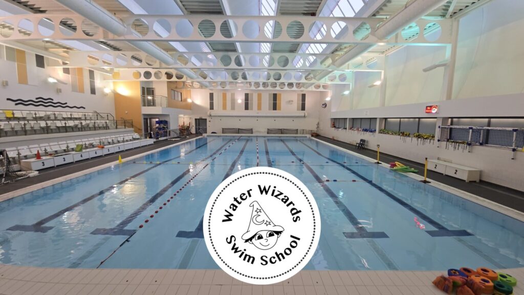 Indoor swimming pool used by Water Wizards Swim School, with lane ropes, poolside seating, and swim equipment visible.